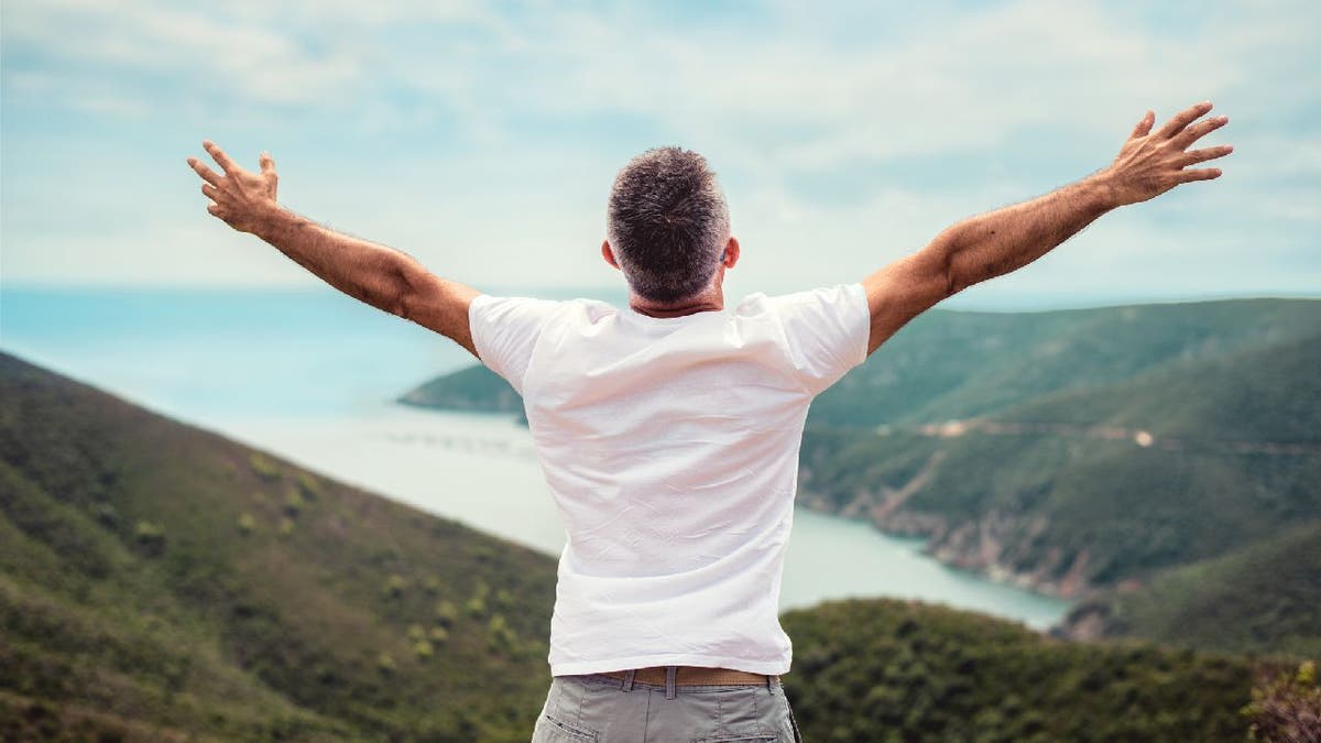 Man outstretches arms outside near cliff