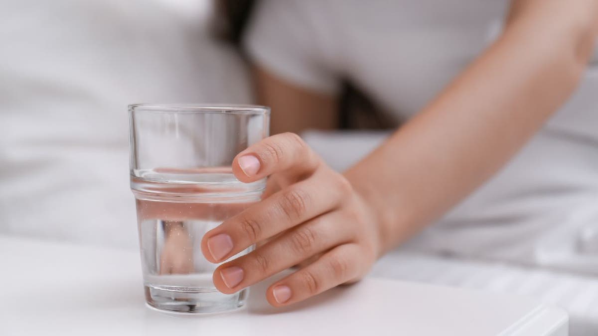 The woman grabs the glass of water near the bed