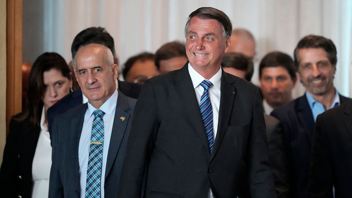 Jair Bolsonaro walks with a smile and a group of men behind him 