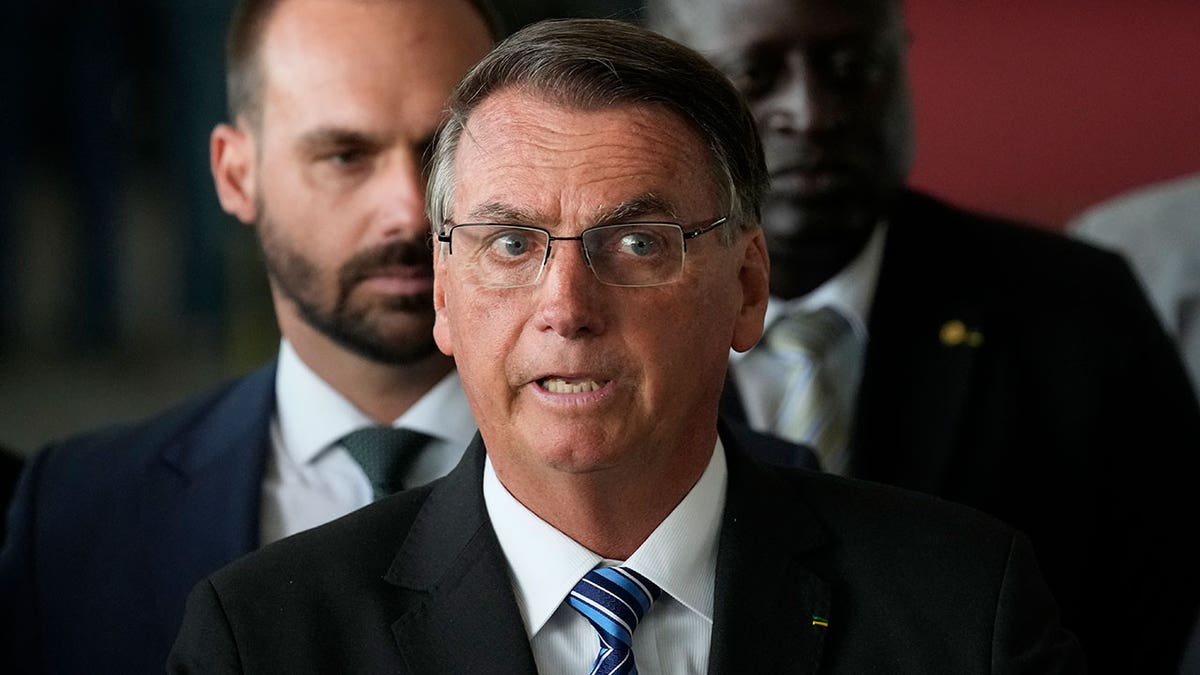 Jair Bolsonaro wears dark suit, blue tie, and glasses as he speaks from his residence