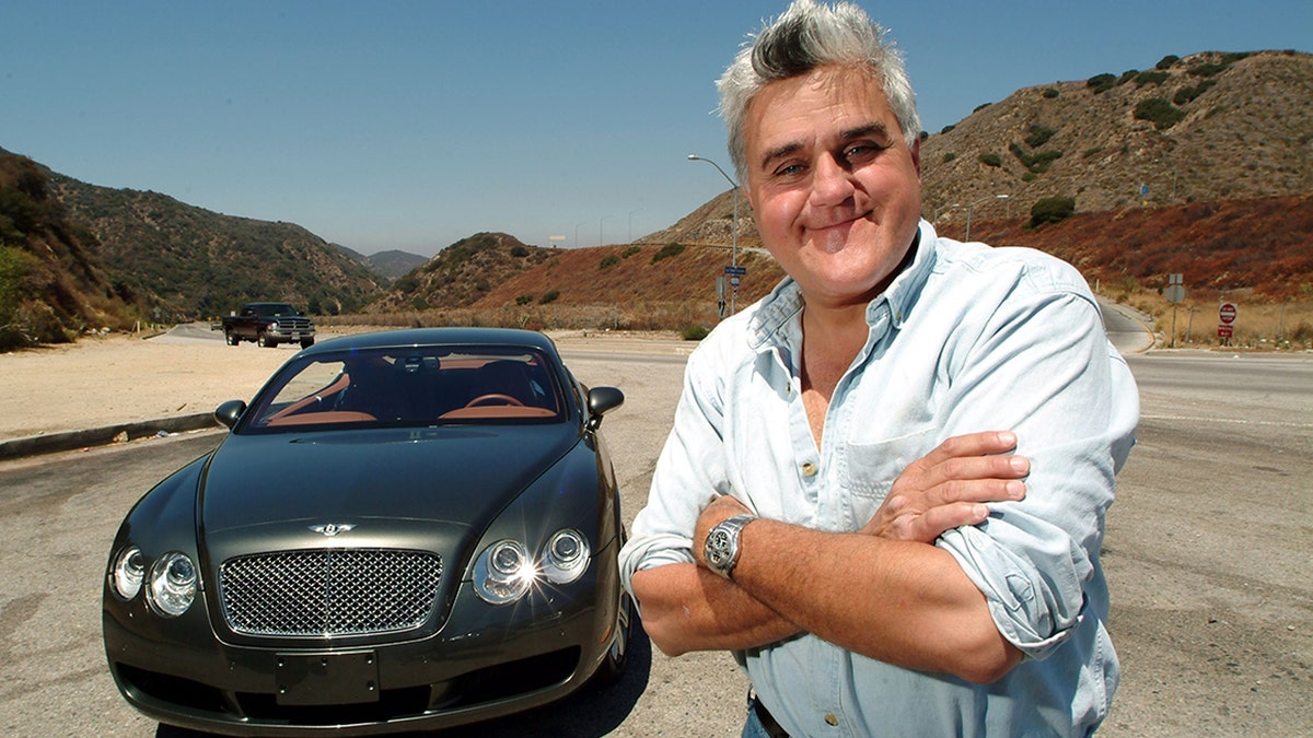 Jay Leno poses next to one of his vintage cars