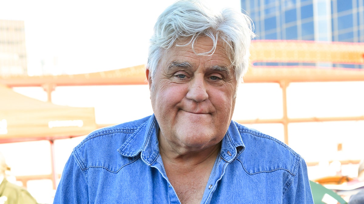 Jay Leno smiles while wearing a blue denim shirt