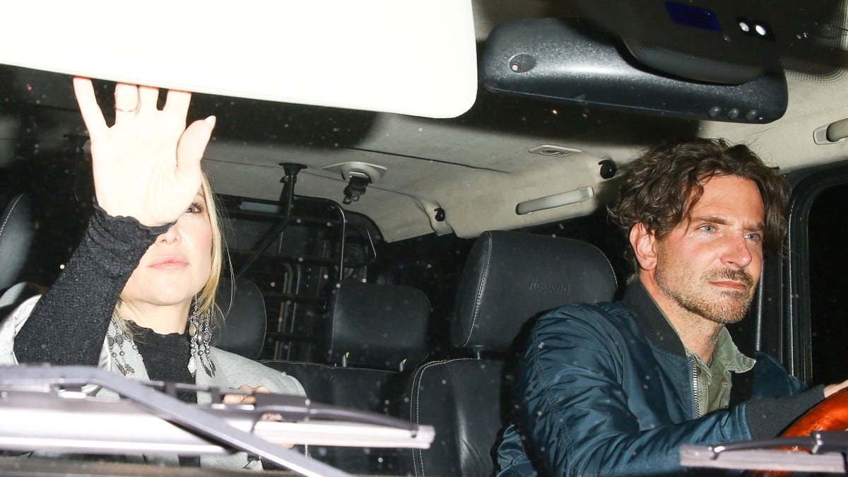 Bradley Cooper drives passenger Kate Hudson who is looking in the mirror to Leo DiCaprio's birthday