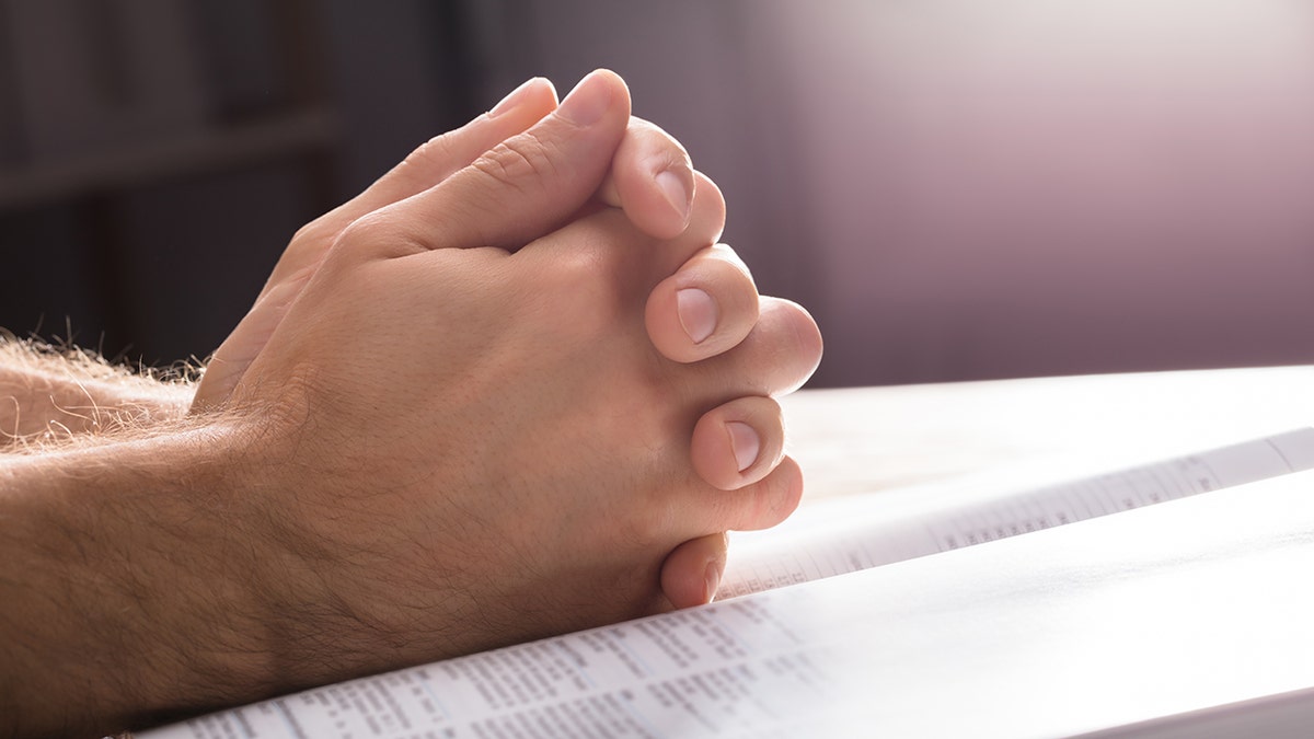 man's hands folded in prayer on Bible