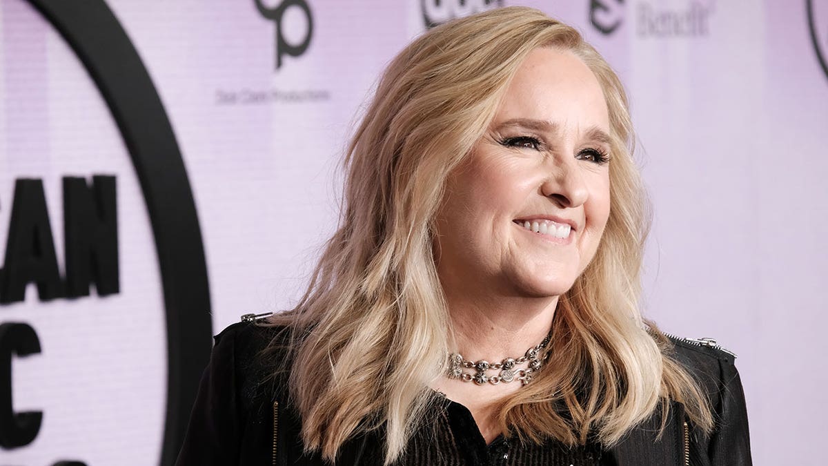 Melissa Etheridge wears an all-black outfit and smiles at the AMA red carpet