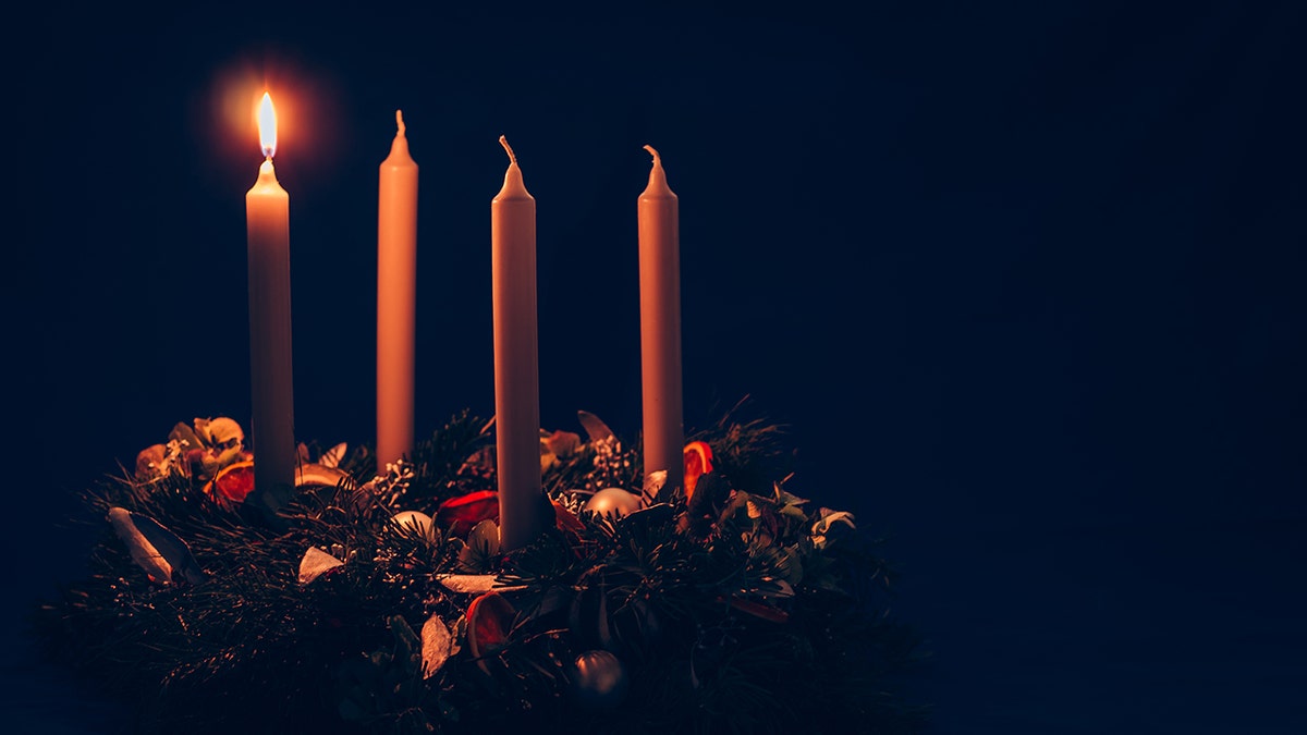 one advent candle lit on a wreath with three more candles