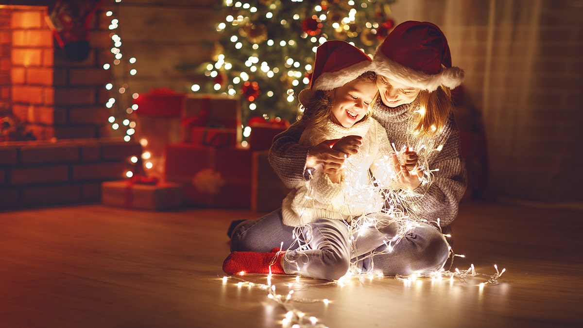 mother and daughter holding Christmas light by tree