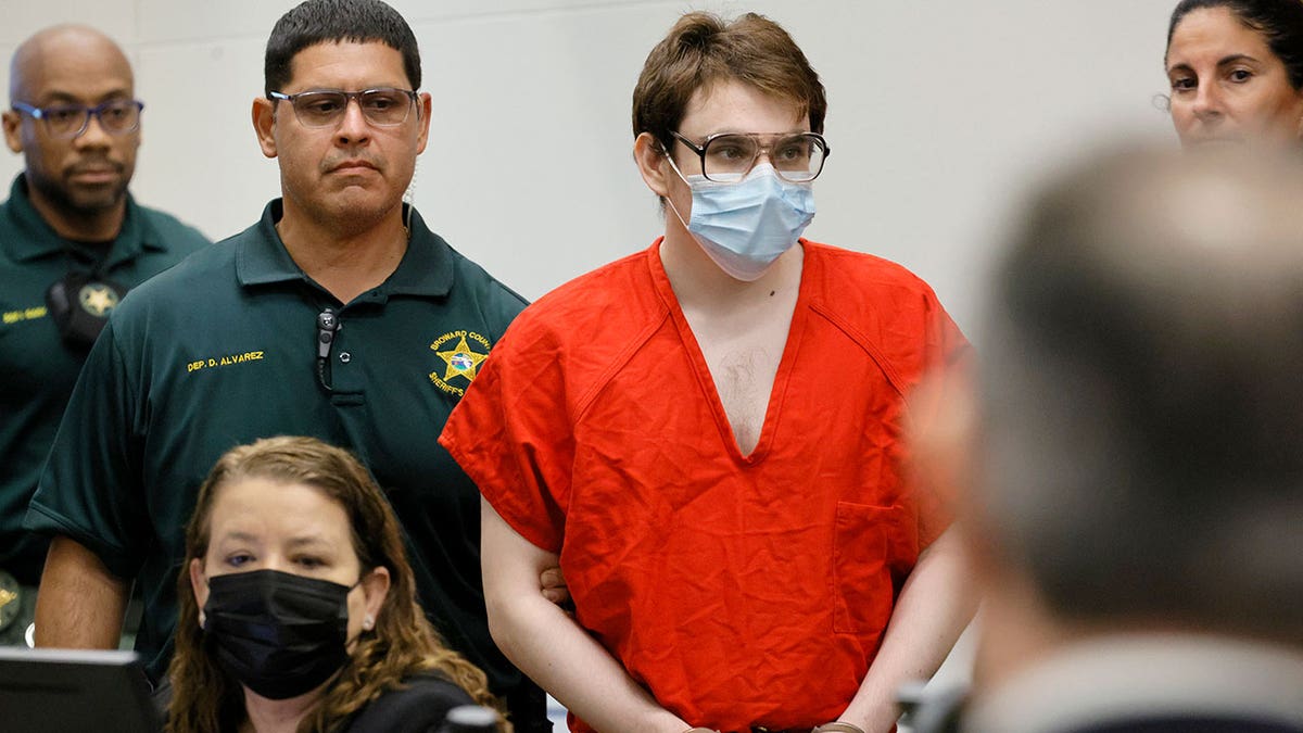Nikolas Cruz is handcuffed, in orange jumpsuit, wearing a mask inside a courtoom