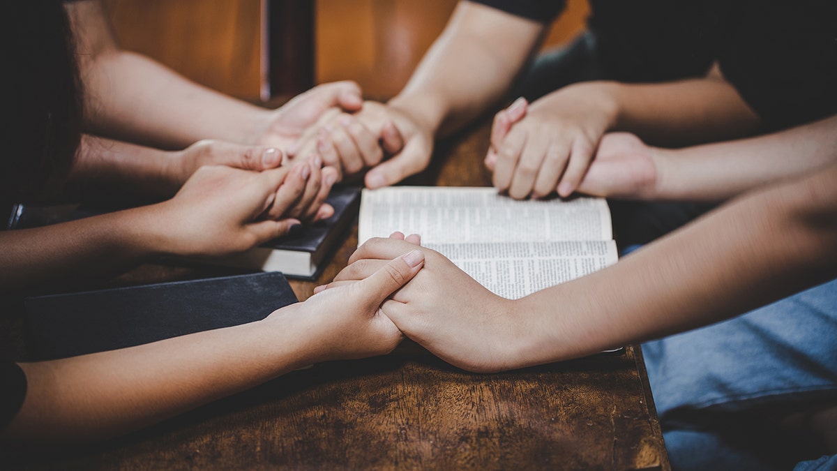hands held in circle in prayer around Bible