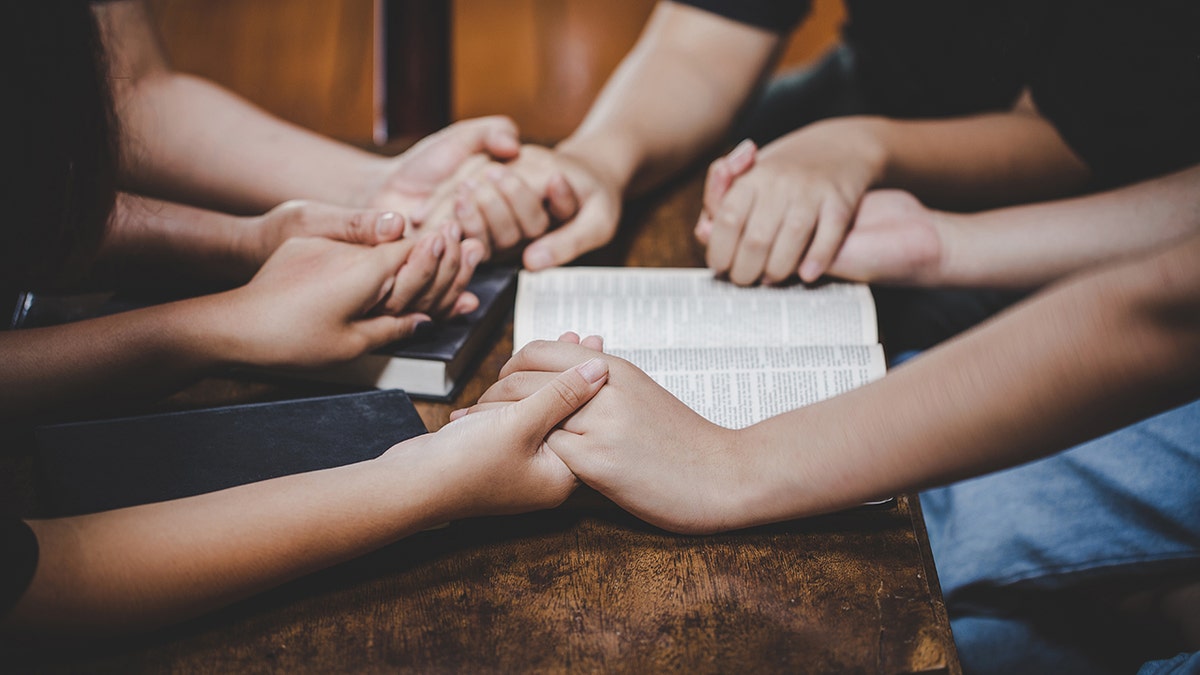 people holding hands in prayer around Bible