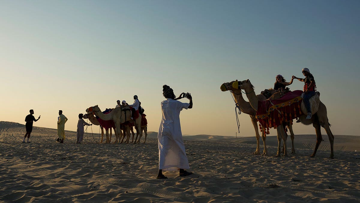 Tourists take selfies while riding camels around sand dunes in Qatar