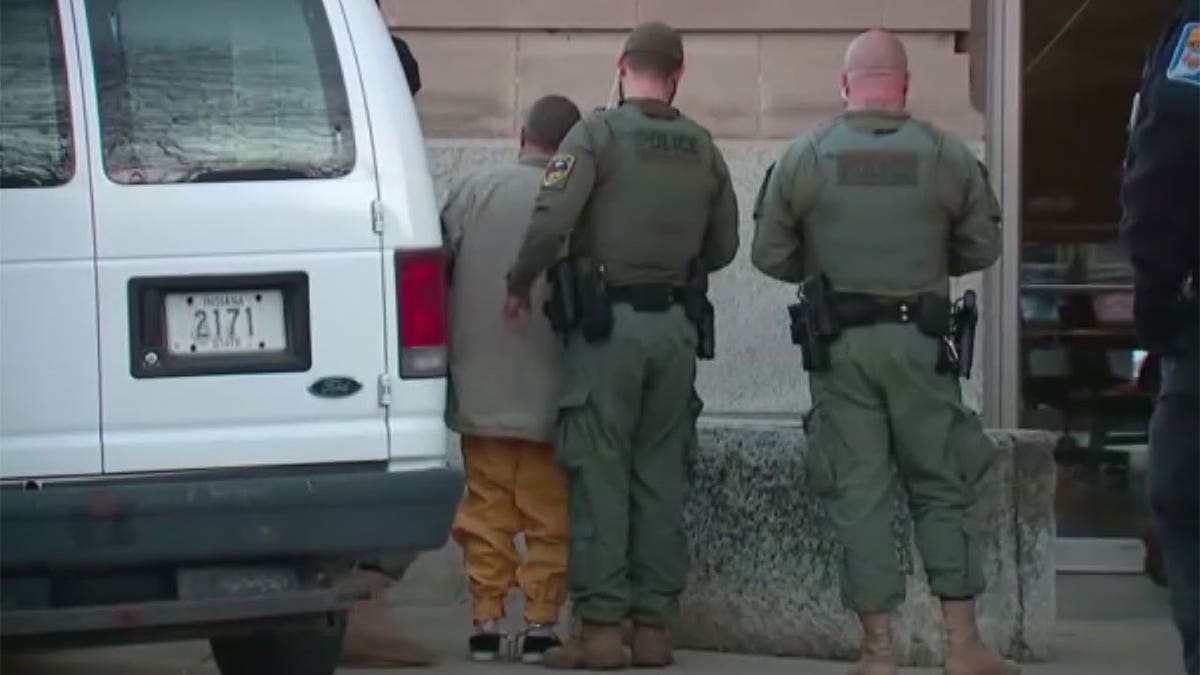 Richard Allen wearing a beige coat and orange jail issue jumpsuit.