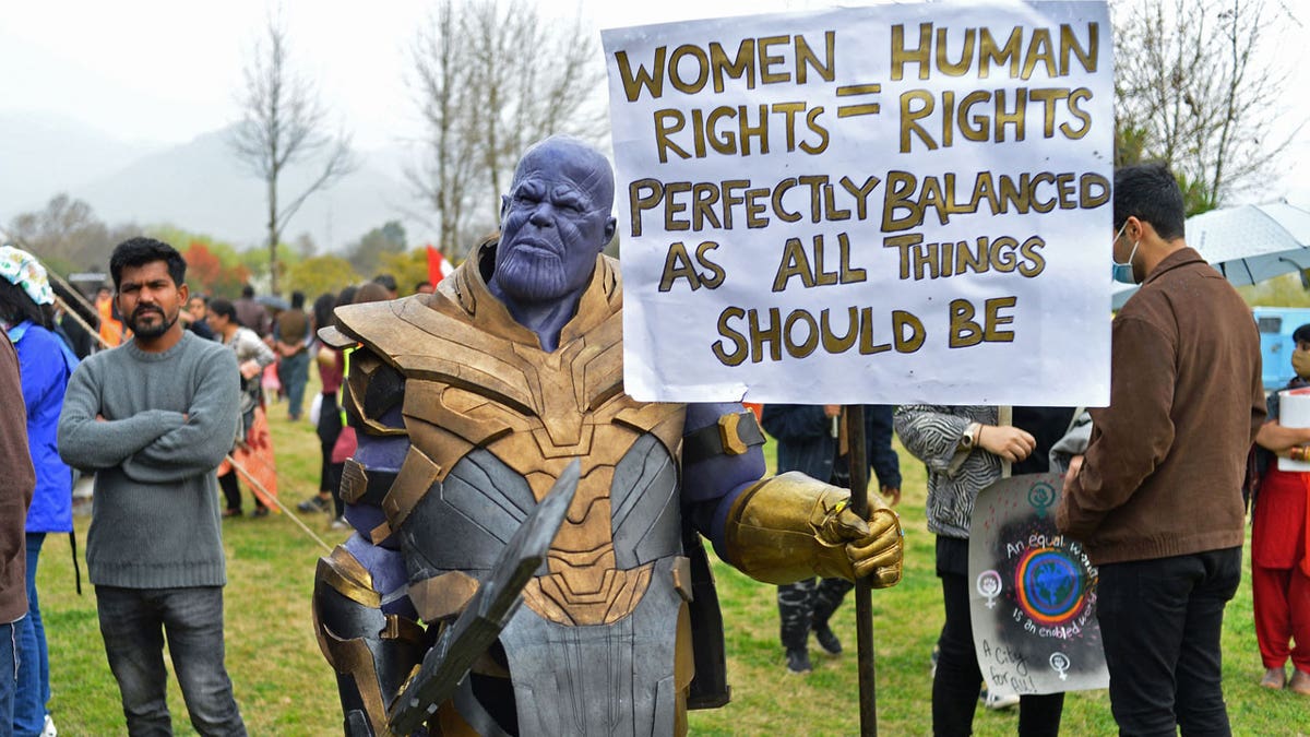 Man dressed up as Thanos holding a sign that reads "women rights = human rights. Perfectly balanced as all things should be"
