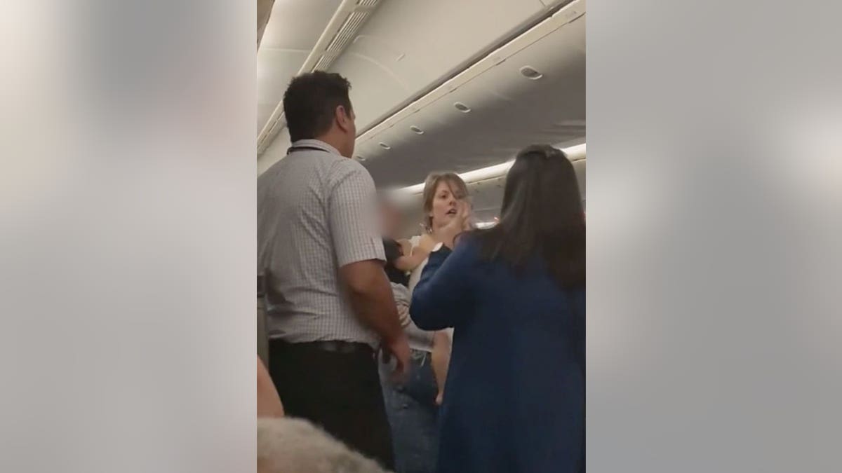 Two flight attendants stand in front of a woman carrying a child on a flight