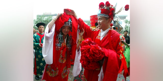 A groom lifts a cloth covering his bride's face during their traditional Chinese wedding ceremony in Beijing May 15, 2004. Some young people in China are going back to their roots for more traditional weddings, and turning away from Western-style ceremonies that had gained popularity.