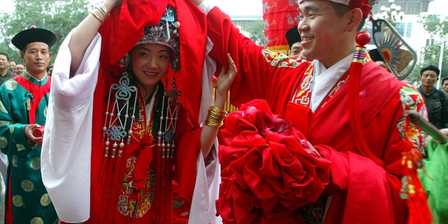 During a traditional Chinese wedding ceremony in Beijing on May 15, 2004, the groom lifts the scarf that covers the bride's face.  Some young people in China are going back to their roots for more traditional weddings and turning away from Western-style ceremonies that have gained popularity.