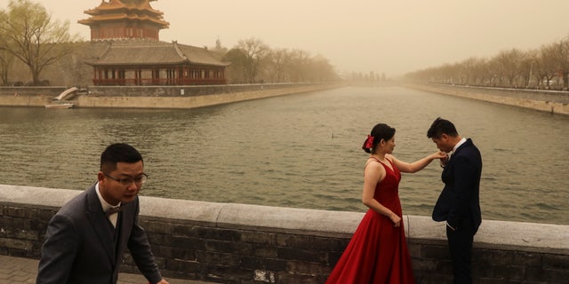 People react when they have wedding photos taken near the Forbidden City in Beijing on March 15, 2021.