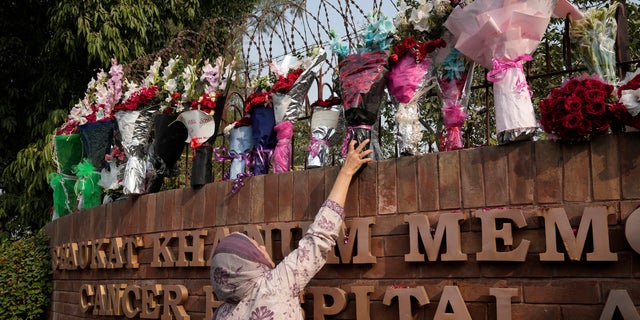 A woman places a bouquet on the wall of a hospital where former Pakistani Prime Minister Imran Khan is being treated for a gunshot wound in Lahore, Pakistan on Friday, November 4, 2022.