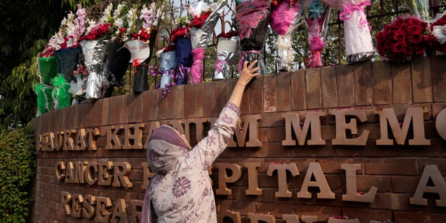 A woman places a bouquet on the wall of a hospital where former Pakistani Prime Minister Imran Khan is being treated for a gunshot wound in Lahore, Pakistan on Friday, November 4, 2022.