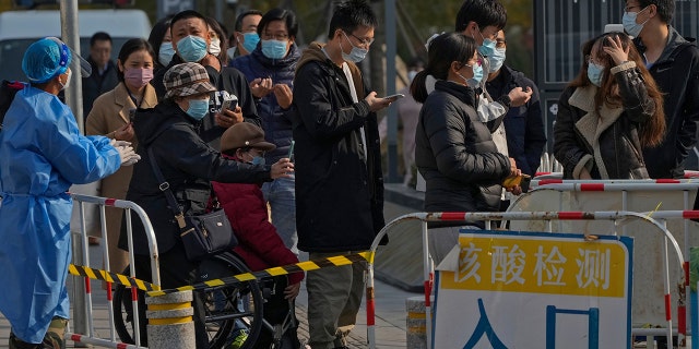 People use their smartphones to scan health check QR codes before receiving their regular COVID-19 throat swabs at a coronavirus testing site in Beijing on Tuesday, November 8, 2022.