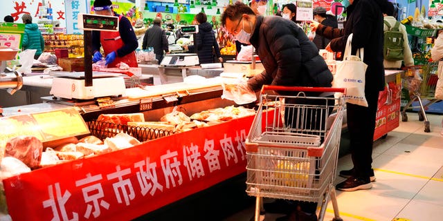 A man wearing a mask shops for meat near a banner which reads "Beijing Government Reserve Meat" for sale at a supermarket in Beijing, Saturday, Nov. 26, 2022. 