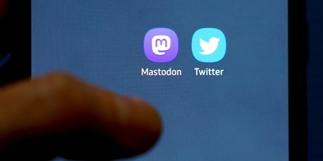 A person holds a mobile phone showing the Mastodon and Twitter icon. 