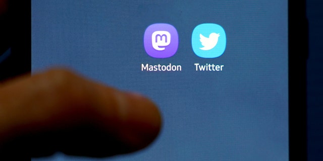 A man holds a mobile phone displaying Mastodon and Twitter icons. 