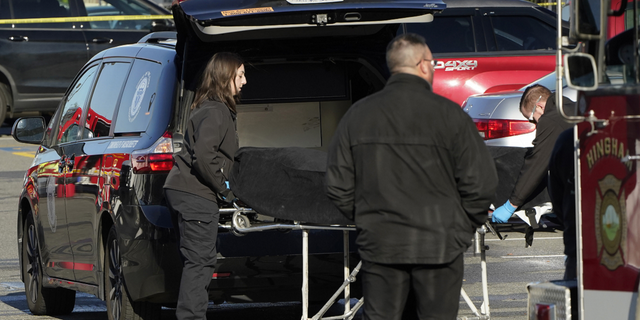 Officials transfer a body into a medical examiner's vehicle outside an Apple store in Hingham, Massachusetts, on Nov. 21.