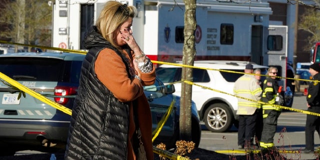 A woman is tearful while standing behind police tape at a scene where an SUV drove into an Apple store, Monday, Nov. 21, 2022, in the Derby Street Shops, in Hingham, Mass. One person was killed and multiple others were injured Monday when the SUV crashed into the store, authorities said. (AP Photo/Steven Senne)