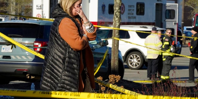 A woman is tearful while standing behind police tape at a scene where an SUV drove into an Apple store, Monday, Nov. 21, 2022, in the Derby Street Shops, in Hingham, Mass. One person was killed and multiple others were injured Monday when the SUV crashed into the store, authorities said. (AP Photo/Steven Senne)