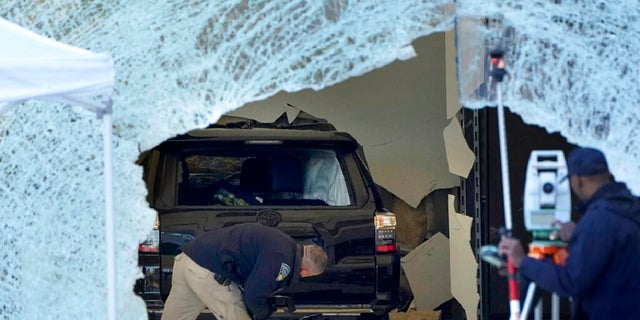 A law enforcement official, center, examines an SUV inside an Apple Store on Monday in Hingham, Massachusetts. The crash left a large hole in the glass front of the Apple Store and killed one person. 