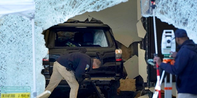 A law enforcement official, center, examines an SUV inside an Apple Store on Monday in Hingham, Massachusetts. The crash left a large hole in the glass front of the Apple Store and killed one person.