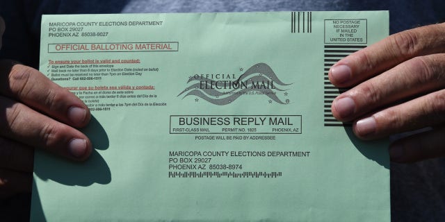 A voter displays their mail-in ballot envelope at an early voting location in Phoenix, Arizona, on Oct. 16, 2020.
