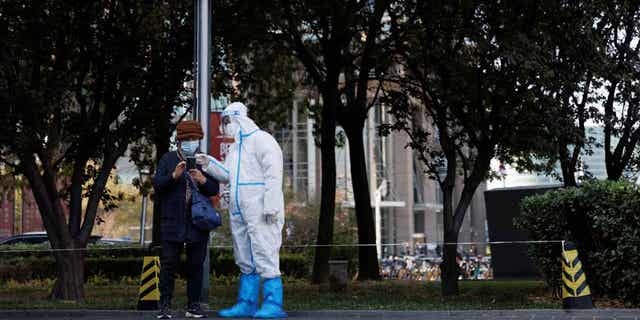 A pandemic prevention worker checks personal details of a woman lining up to get a swab test at a testing booth in Beijing, China, Nov. 3, 2022.