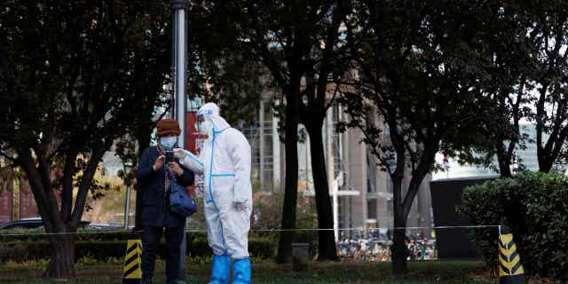 A pandemic prevention worker checks the personal details of a woman lined up to undergo a swab test as coronavirus outbreaks continue in Beijing, China on November 3, 2022. 