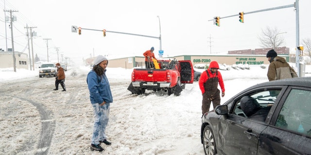 Hakim Grant removes a chain from his truck as Kevin Jones, left, Brandon Burt, center, and Karim Abdullah assess the snow situation around Ploe Kaw's car at Bailey and William Street in Buffalo, N.Y., Friday, Nov. 18, 2022. Grant and his friends pulled over when they saw Kaw, who lives on the West Side, stuck in the snow. 