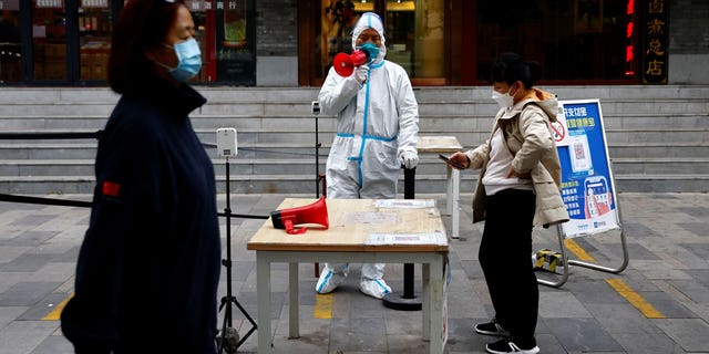 A worker in a protective suit guides people to scan QR health code before taking a COVID-19 test at a testing booth, in Beijing, China Oct. 27, 2022.
