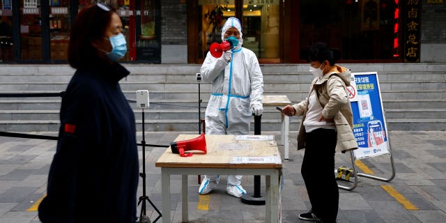 A worker in protective suit guides people to scan the QR health code before performing a COVID-19 test in a test booth, in Beijing, China on Oct.27, 2022.