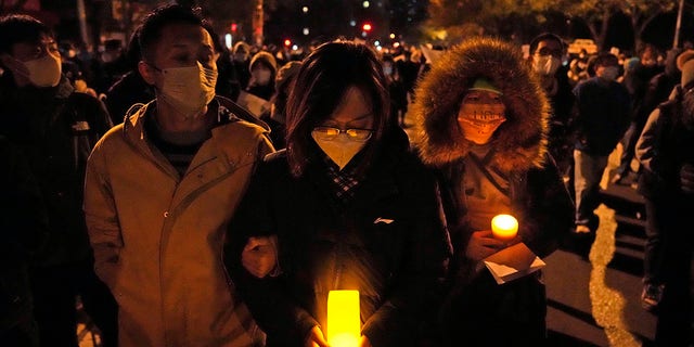 Manifestantes seguram velas enquanto marcham em Pequim após os protestos de COVID-19 em todo o país.