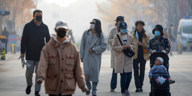 People wearing face masks walk along a pedestrian shopping street at the Wangfujing shopping district in Beijing, Saturday, Nov. 19, 2022.