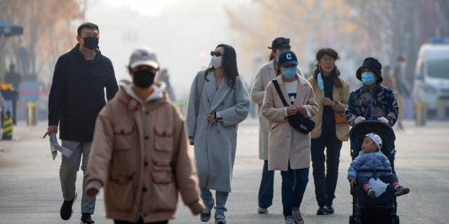 People wearing face masks walk along a pedestrian shopping street in Beijing's Wangfujing shopping district on Saturday, Nov. 19, 2022.