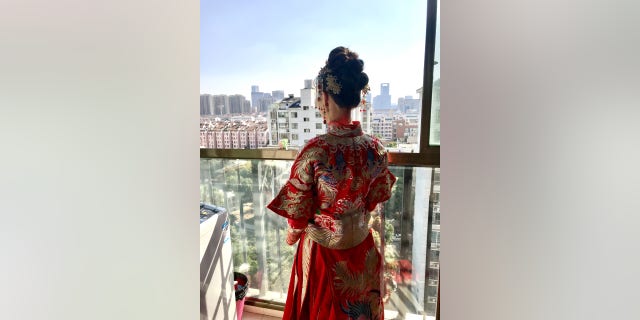 A Chinese bride wearing a traditional red wedding dress gazes over her city prior to her wedding ceremony.