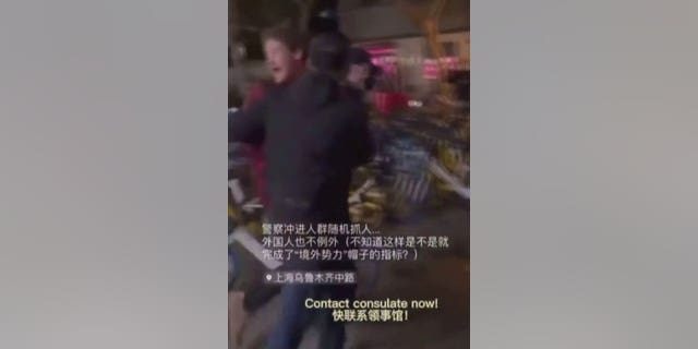 Chinese law enforcement walking the BBC reporter away as he yells out to contact the consulate in Shanghai.