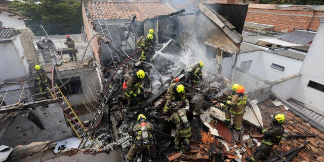 Firefighters work at the crash site of a small plane that crashed into homes in a residential area of Medellin, Colombia, on November 21, 2022.