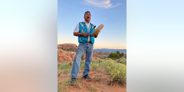 A man beats a drum as the sun sets over the vast New Mexico landscape.