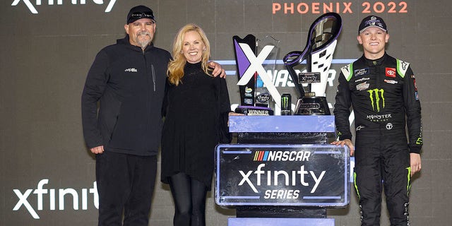 تای گیبز، راننده تویوتای هیولا انرژی شماره 54، با پدرش، کوی گیبز و مادرش، هدر گیبز، در مسیر پیروزی پس از برنده شدن در مسابقات قهرمانی سری Xfinity NASCAR در فینیکس ریس وی در 5 نوامبر 2022 در آوندیل، آریزونا جشن می گیرد.