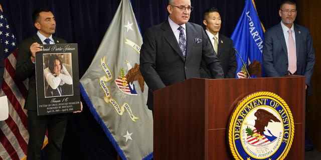 United States Attorney Martin Estrada, left, holds a picture of the late Daniel Puerta-Johnson, 16, a victim of Fentanyl poisoning, as his father, Jaime Puerta, president of Victims of Illicit Drugs, at the podium, joins the U.S. Attorney's Office Central District of California office to address the widespread damage caused by fentanyl in Los Angeles, on Monday, Nov. 21.