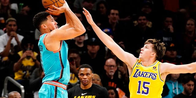 Phoenix Suns' Devin Booker, left, shoots a three pointer against Los Angeles Lakers' Austin Reaves, #15, during the first half of an NBA basketball game in Phoenix, Tuesday, Nov. 22, 2022. 
