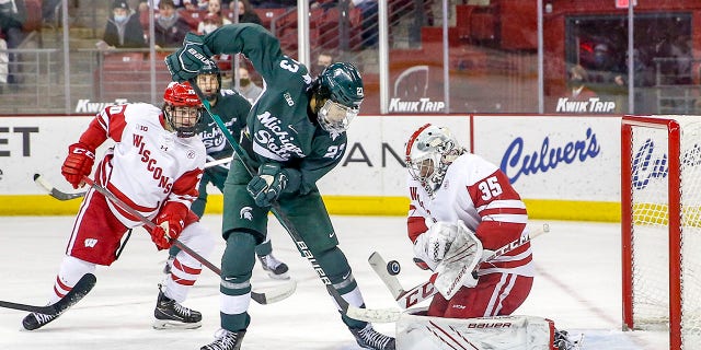 Wisconsin goalie Jared Moe, #35, makes a save while Michigan State forward Jagger Joshua, #23, goes for a rebound during a college hockey game between the University of Wisconsin Badgers and the Michigan State University Spartans on January 14, 2022 at the Kohl Center in Madison, Wisconsin.