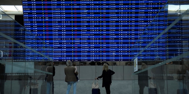 This photograph, taken on September 16, 2022, shows travelers looking at the departure information panel at Roissy-Charles de Gaulle Airport Terminal 2. 